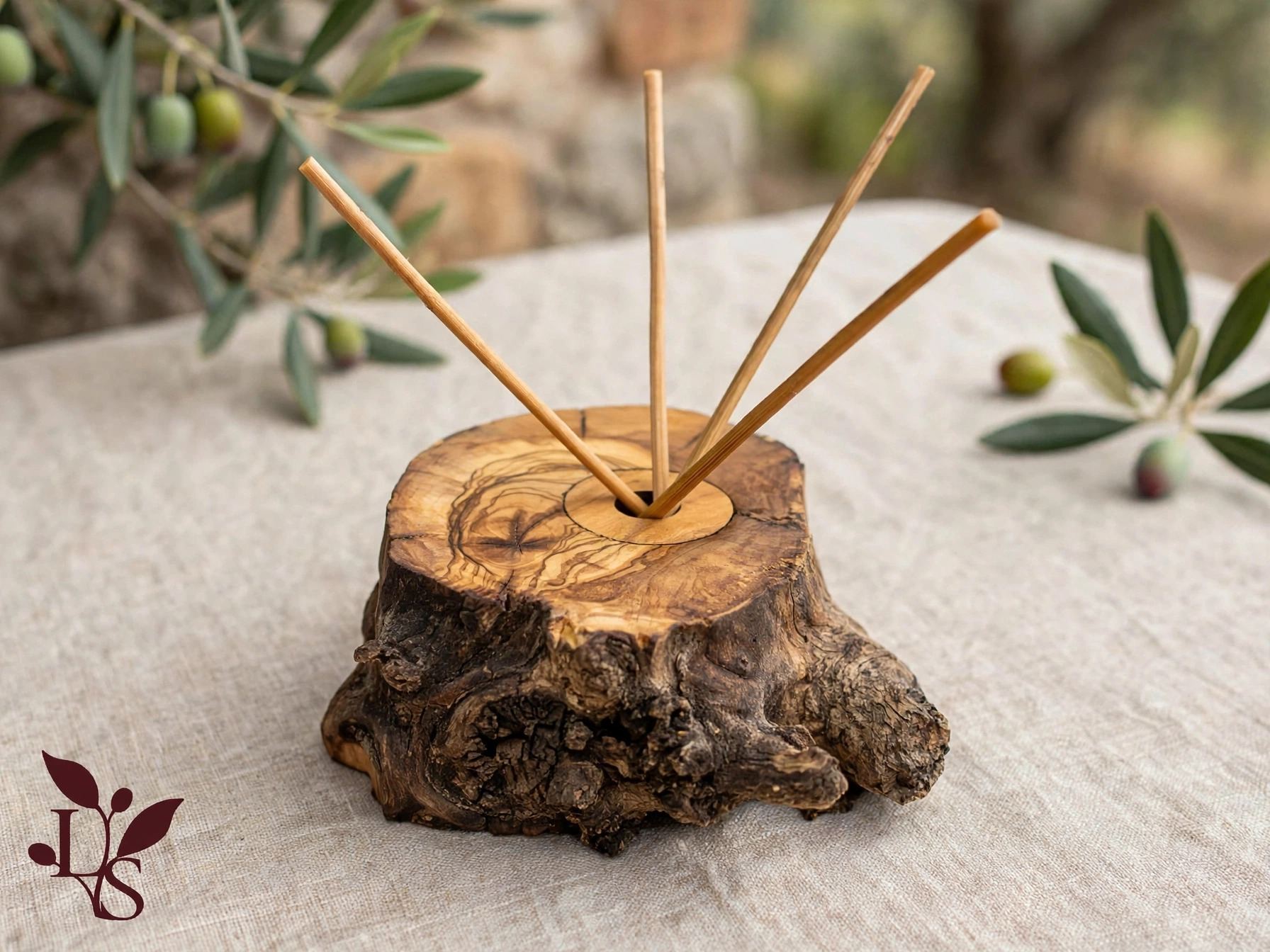 Finished olive wood diffuser with reed sticks, resting beside an olive branch