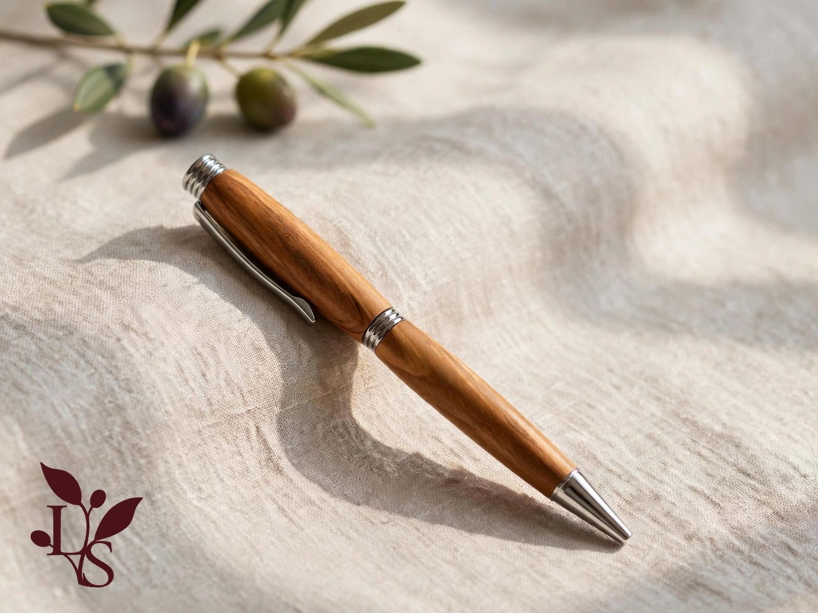 Finished olive wood pen with the Lavinia Seracini mark, resting on linen beside an olive branch