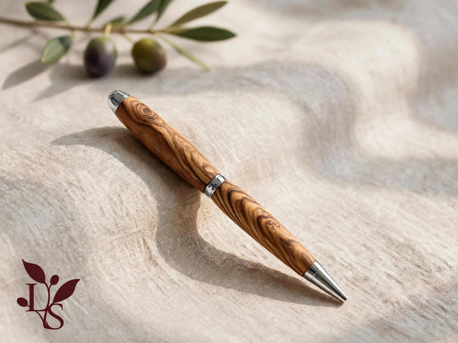 Olive wood pen with chrome fittings on linen beside an olive branch
